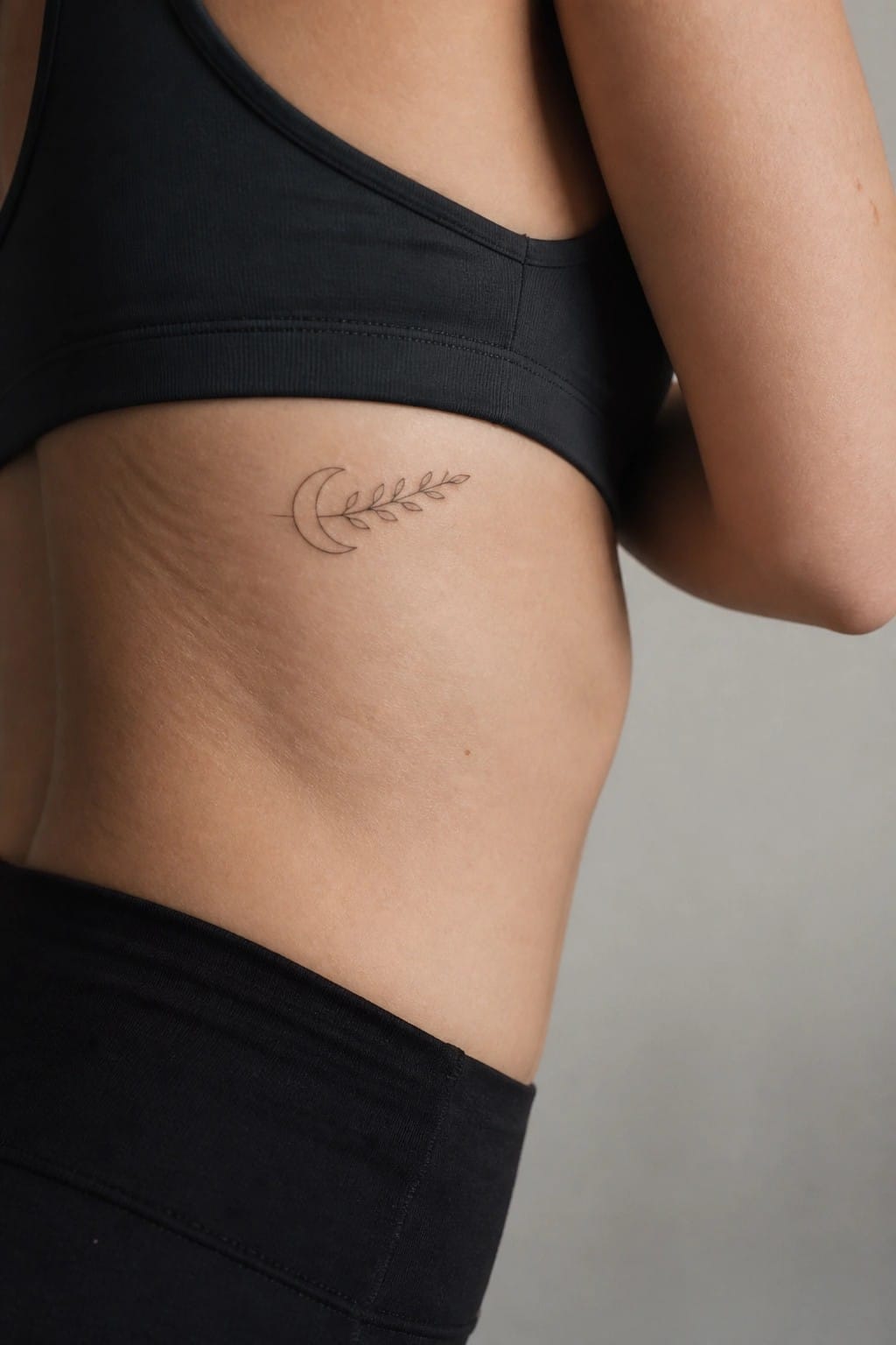 Crescent moon and leafy branch tattoo on torso near black sports bra