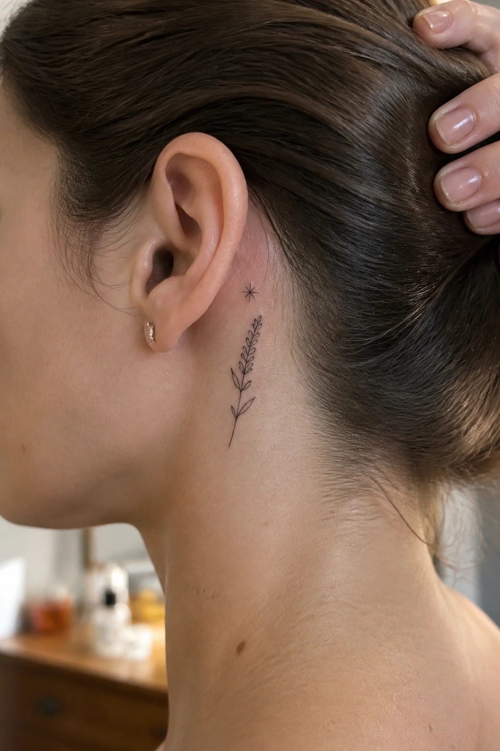Woman with brown hair in bun, leafy plant tattoo and star behind ear