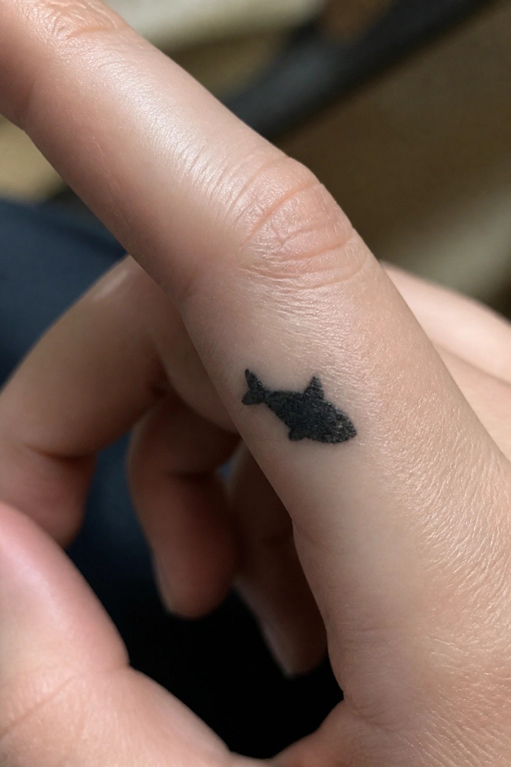 Close-up of small black fish tattoo on light-skinned finger side