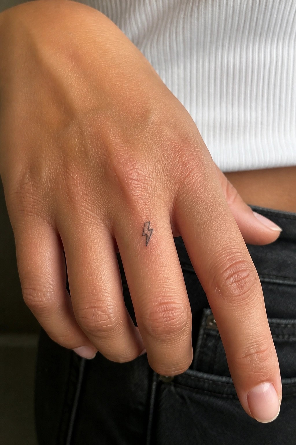 Hand with small lightning bolt tattoo on ring finger, white top and black pants