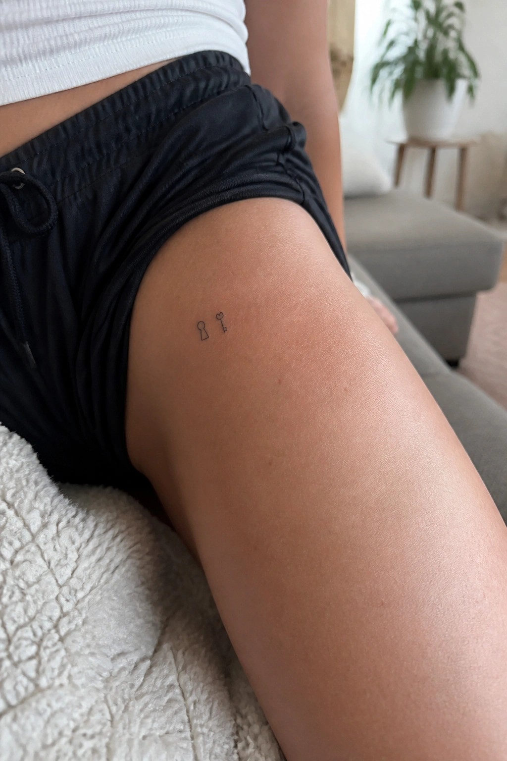Thigh with small lock and key tattoo, black shorts and white crop top.