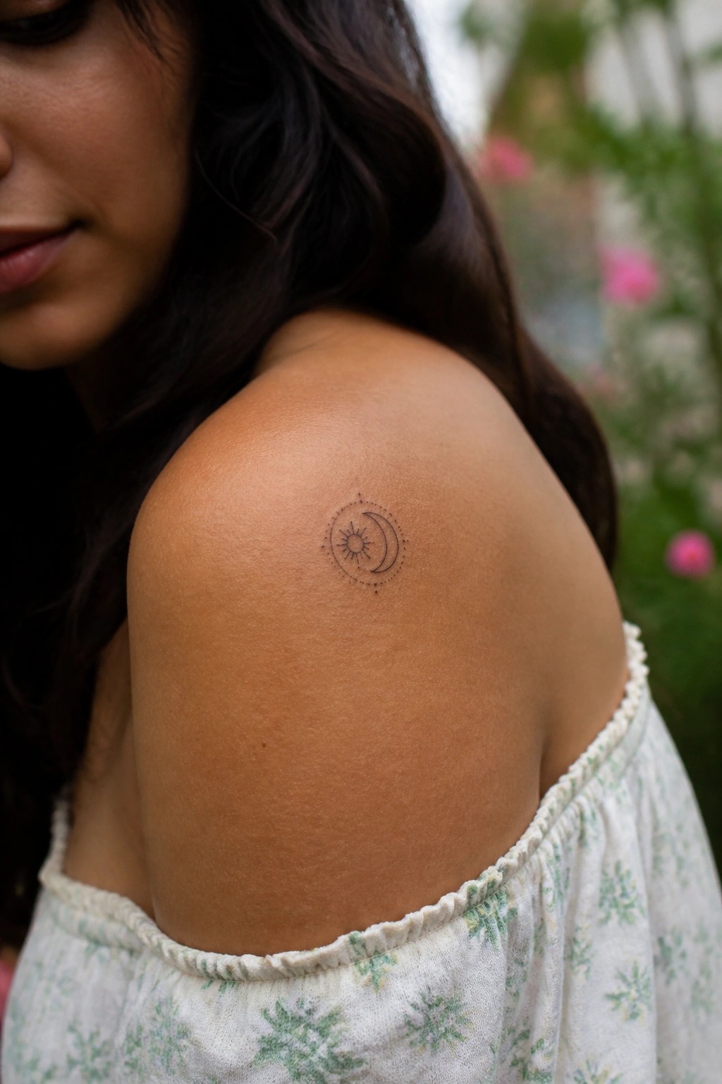 Sun and moon tattoo on shoulder of woman in white floral off-shoulder top