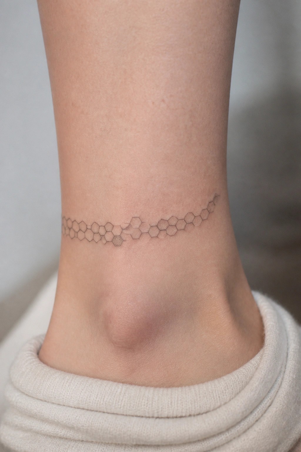 Geometric hexagonal tattoo band on ankle above white ribbed sock