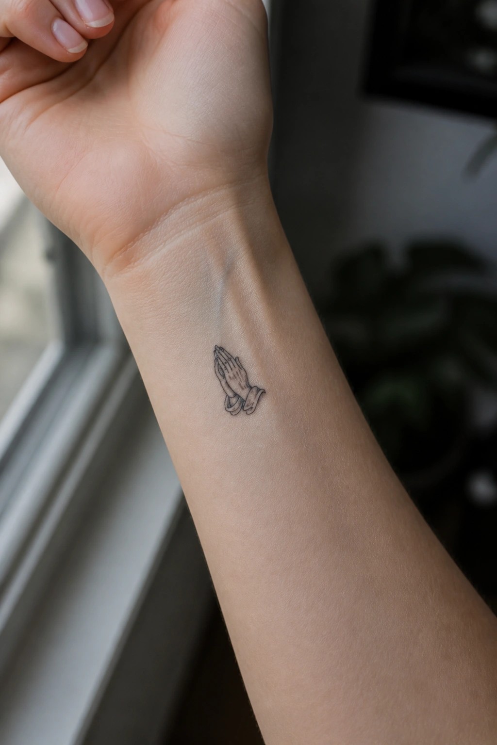 Small line drawing of praying hands tattooed on the inner wrist