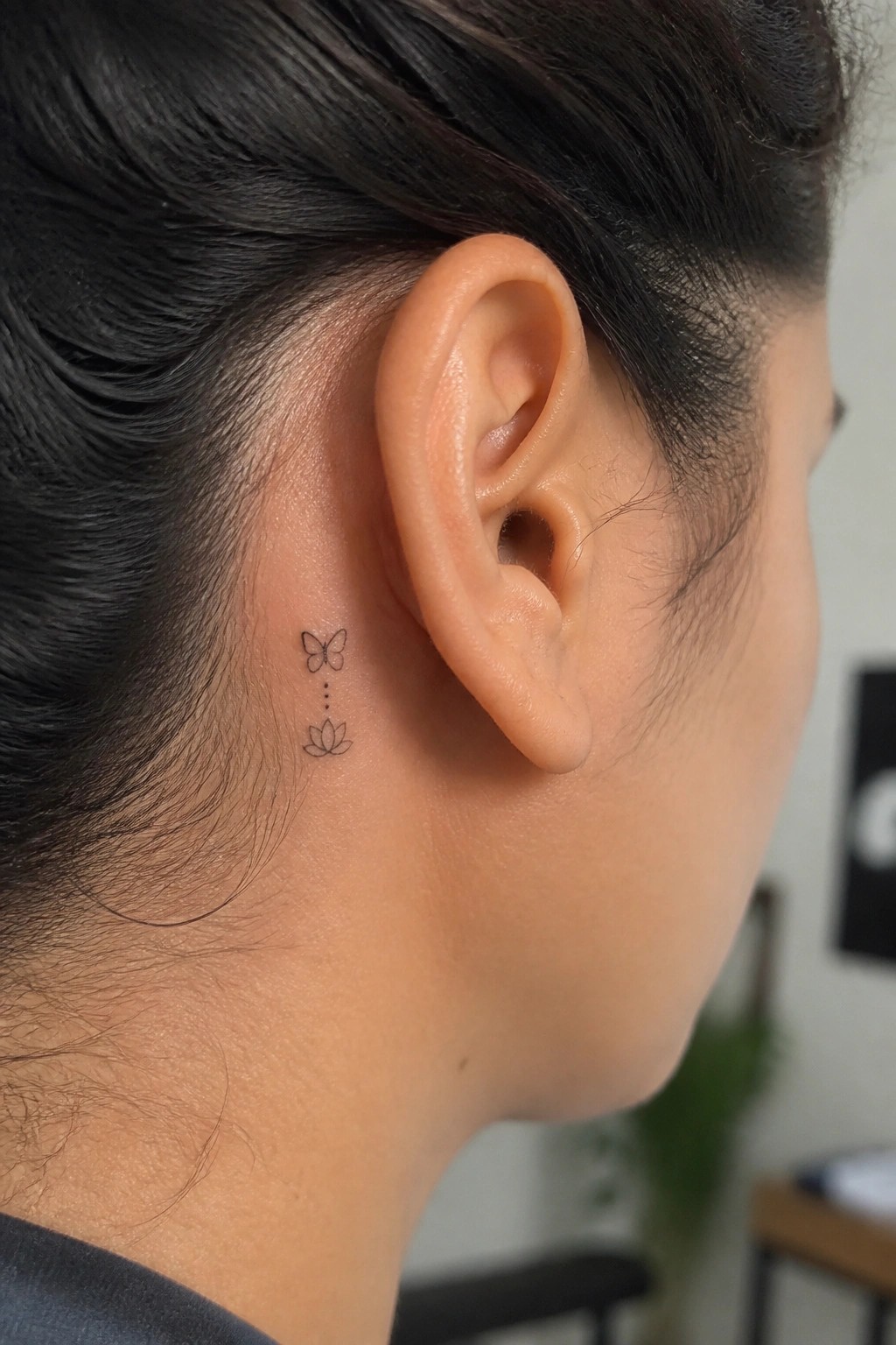 Small butterfly, dots, and lotus tattoo behind a person's ear.