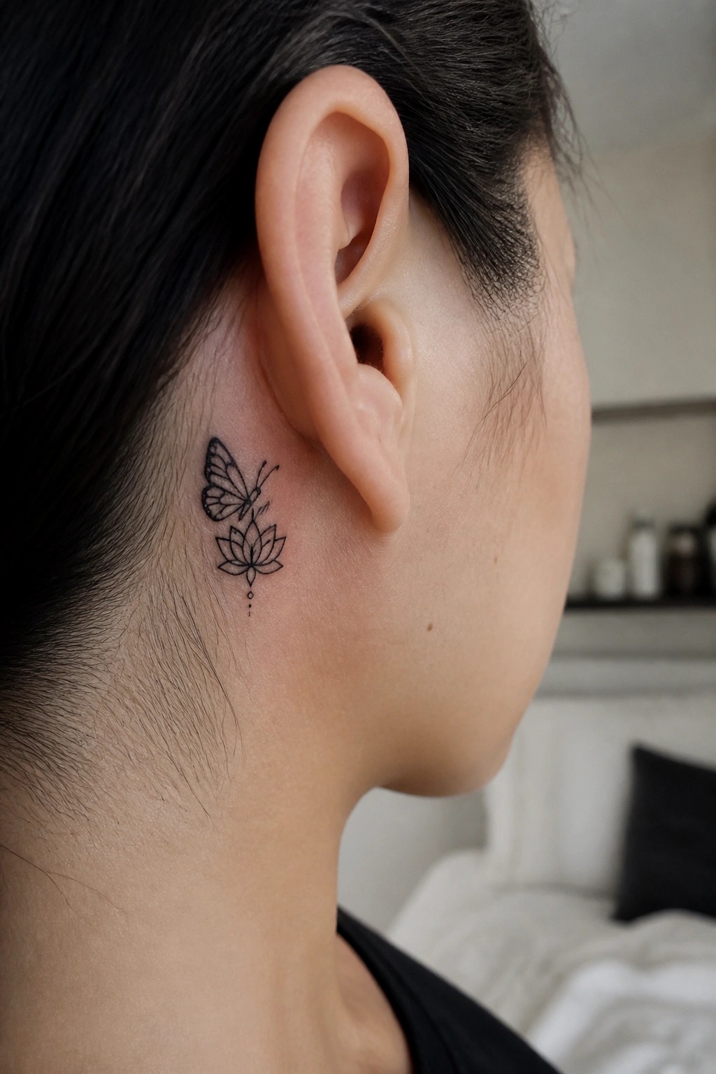 Minimalist black butterfly and lotus flower tattoo behind the ear
