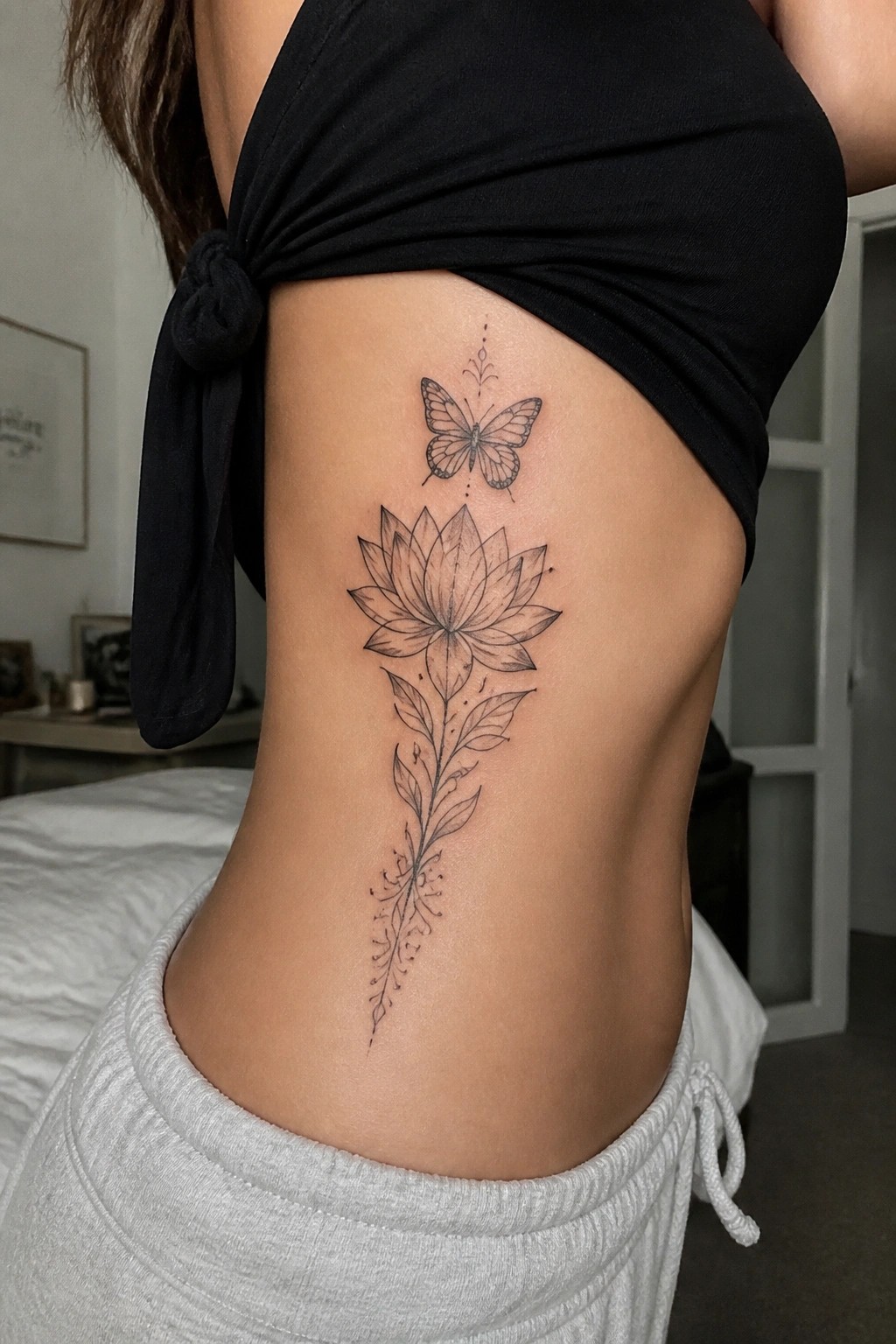 Black knotted top and gray pants frame lotus butterfly tattoo on side torso.