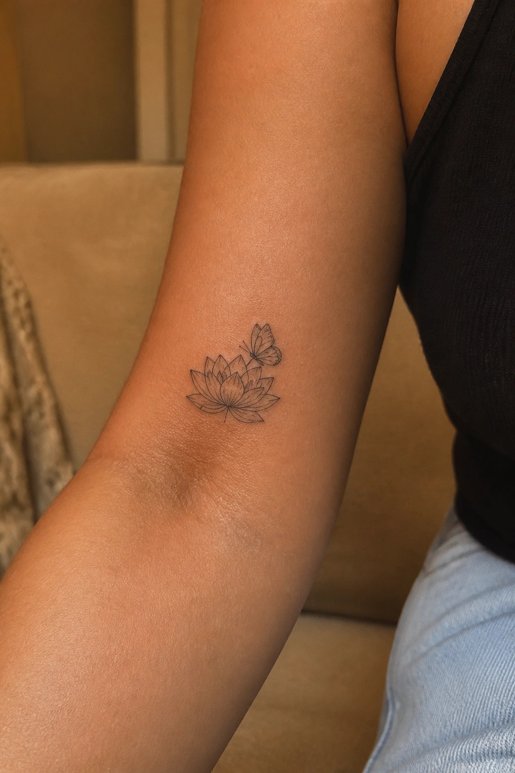 Lotus flower and butterfly tattoo on forearm beside black top and blue jeans
