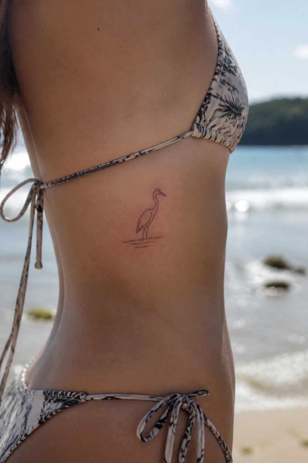 Woman's ribcage with small bird tattoo in patterned bikini at beach