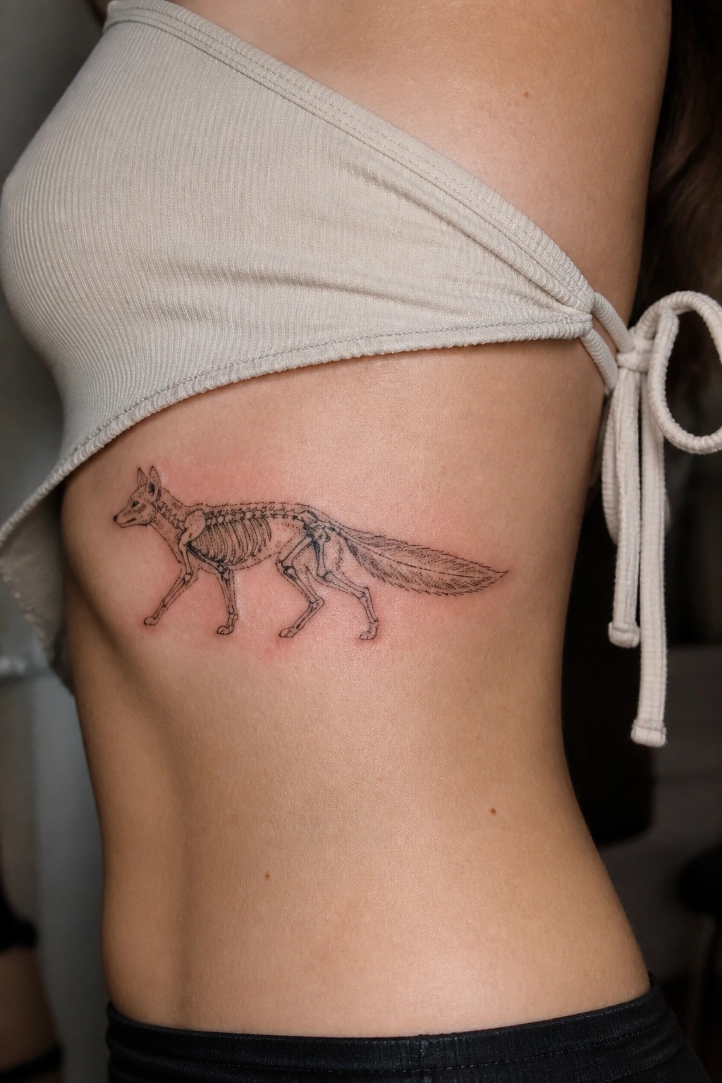 Beige tied crop top revealing walking fox skeleton tattoo on bare midriff