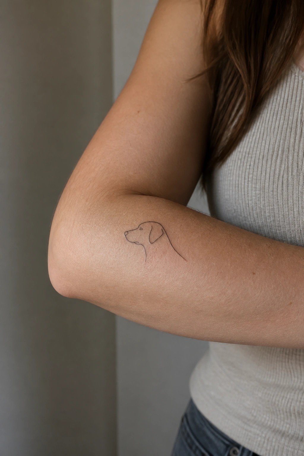 Minimalist line art tattoo of a dog's head on a woman's inner forearm