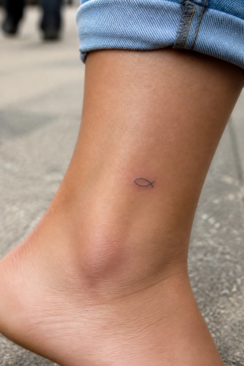 Small fish tattoo on ankle below rolled-up blue denim jeans cuff