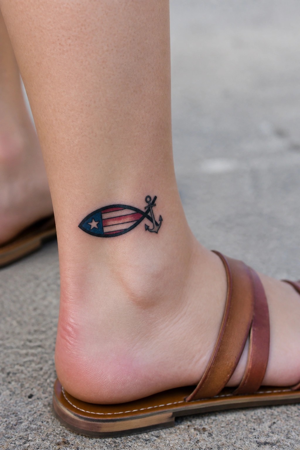Ankle tattoo of fish with American flag design and anchor beside brown sandal.