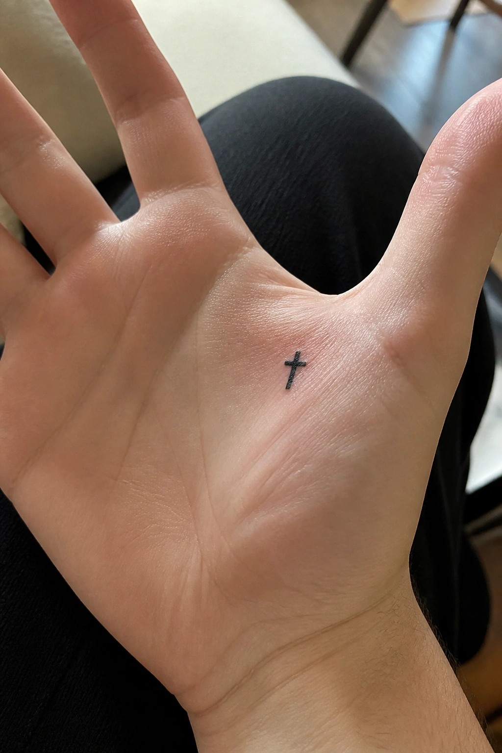 Open hand with small black cross tattoo centered on the palm.