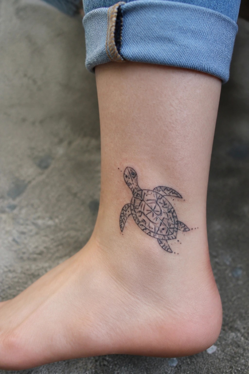 Geometric sea turtle tattoo on ankle below cuffed blue jeans on bare foot