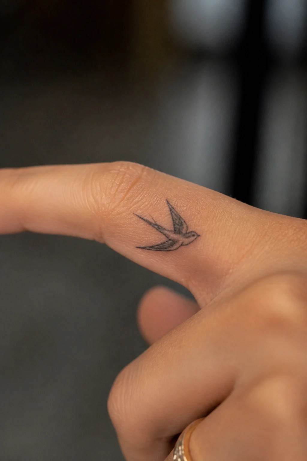 Tiny black swallow tattoo on the side of an index finger