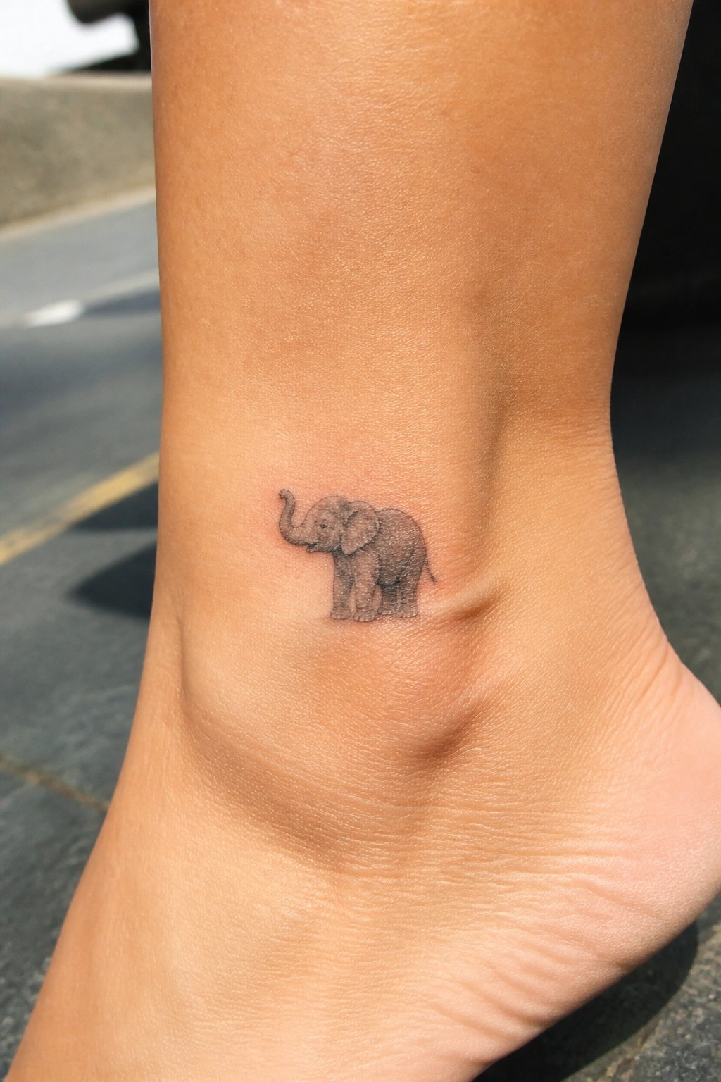 Small black-and-gray elephant tattoo with raised trunk on ankle skin