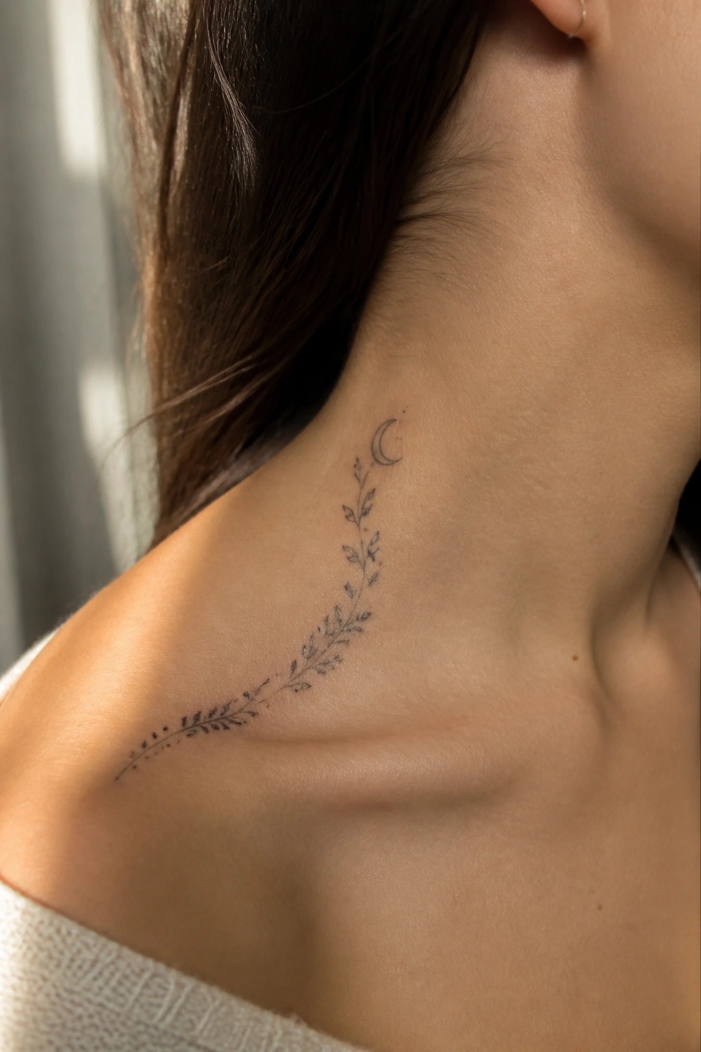 Crescent moon and leafy vine tattoo curving down a woman's neck and shoulder