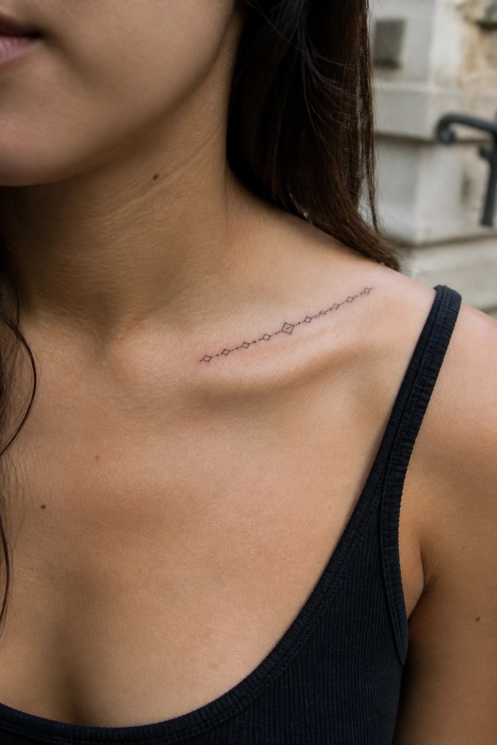 Woman's collarbone with geometric diamond tattoo above black ribbed tank top
