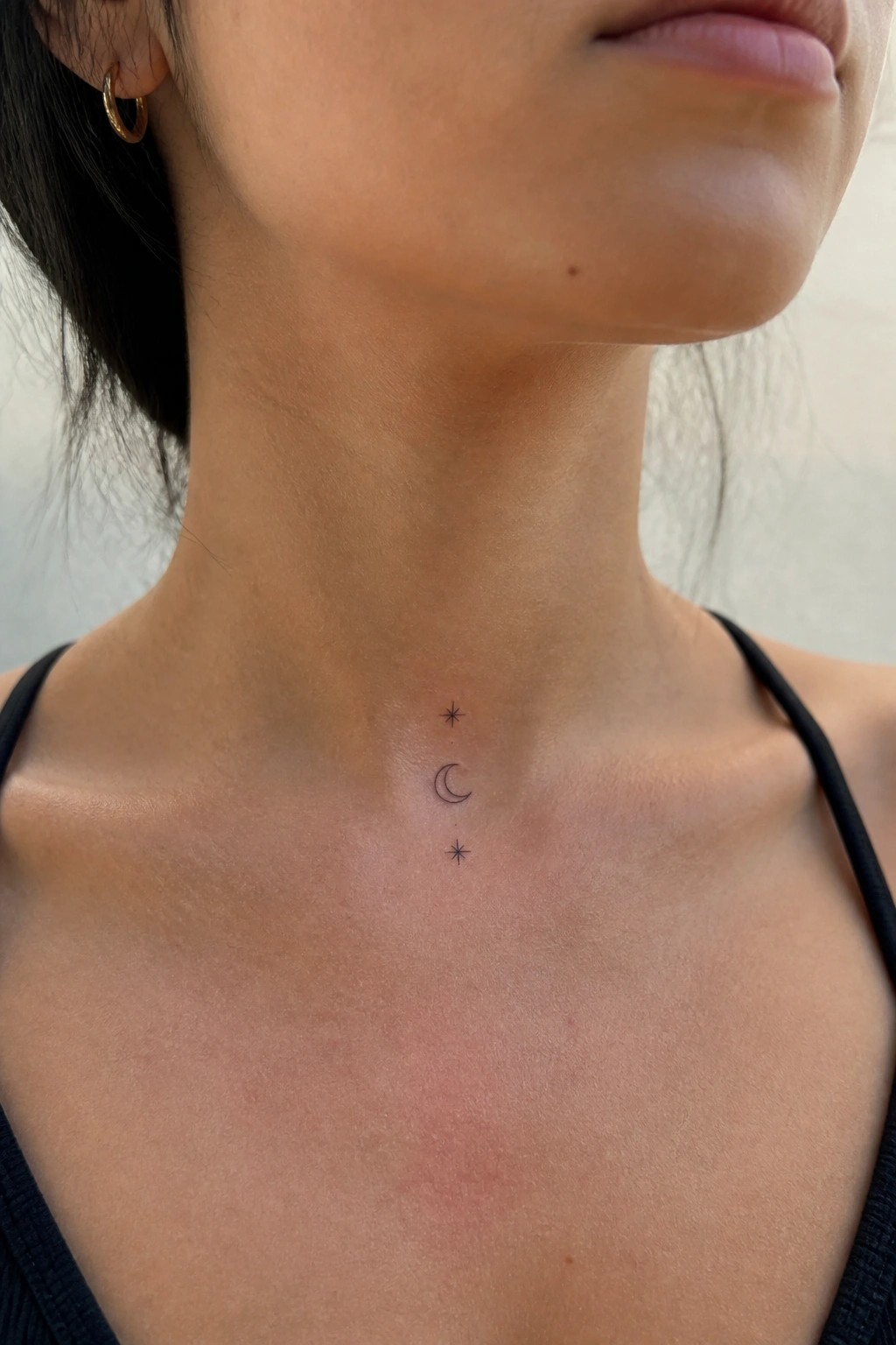 Minimalist crescent moon and stars tattoo on neck above black tank top straps.