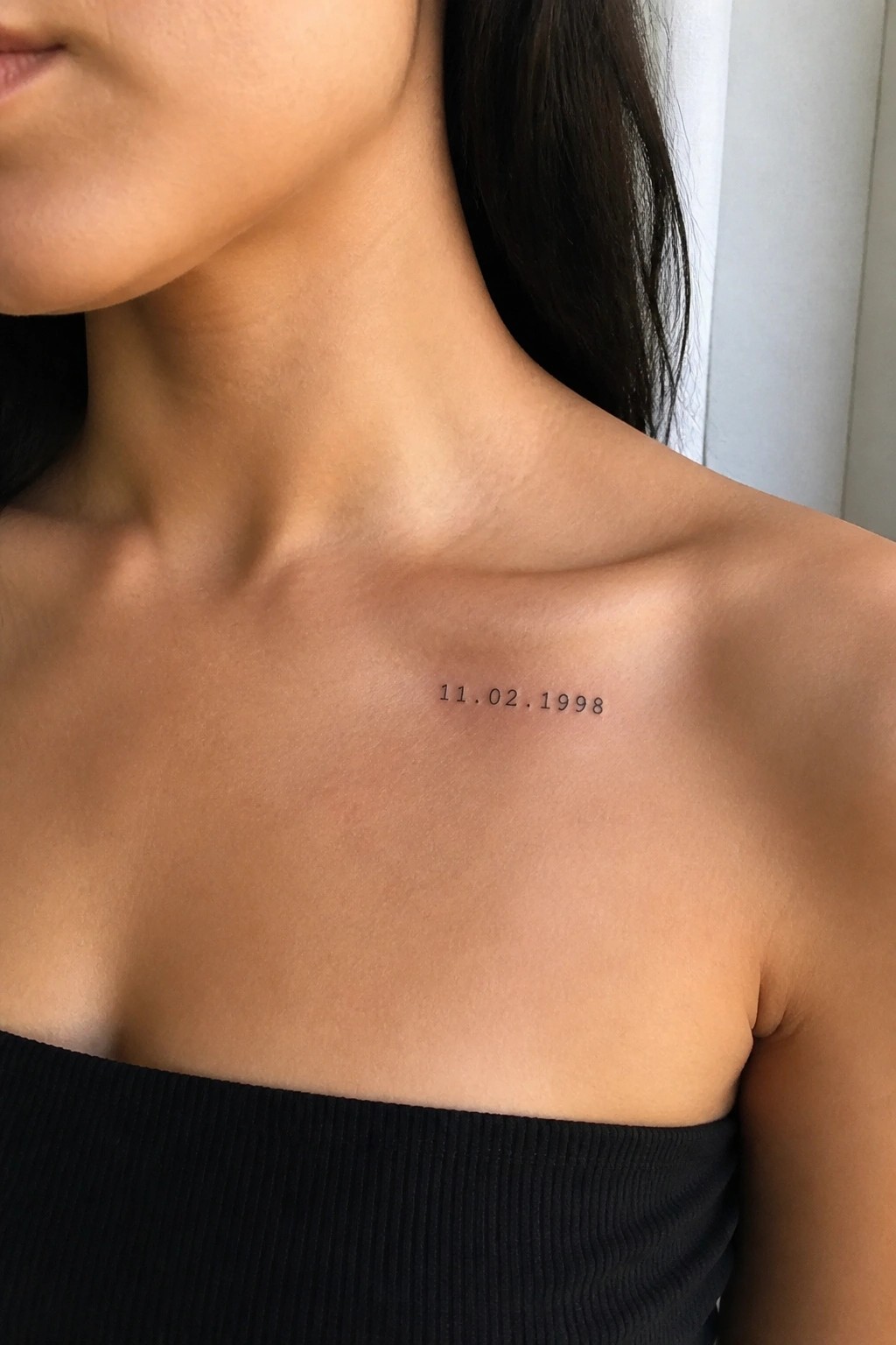 Black date tattoo 11.02.1998 on light skin above black strapless top