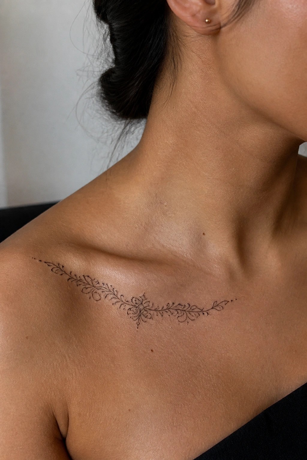 Delicate symmetrical floral tattoo on bare collarbone and shoulder with dark hair