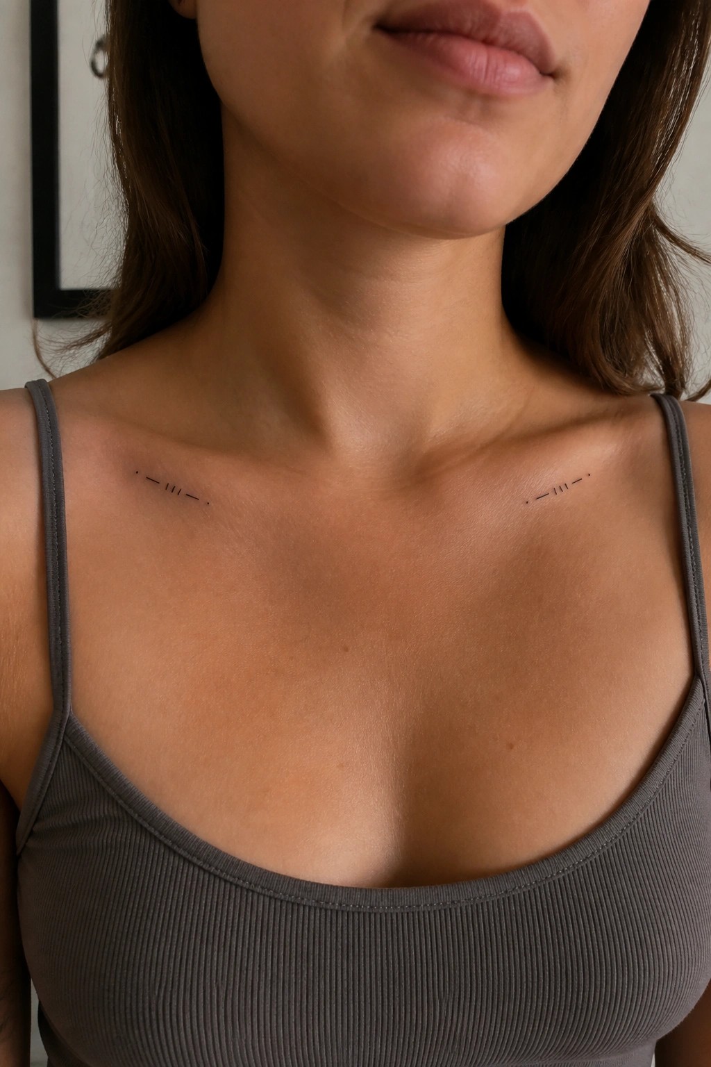 Woman in gray tank top with small black dot-dash tattoos on collarbones.