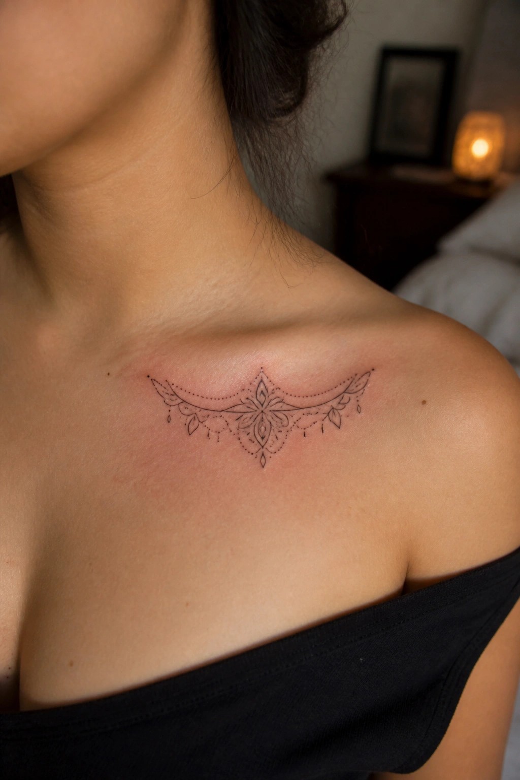 Ornate black mandala tattoo on reddened collarbone above black off-shoulder top