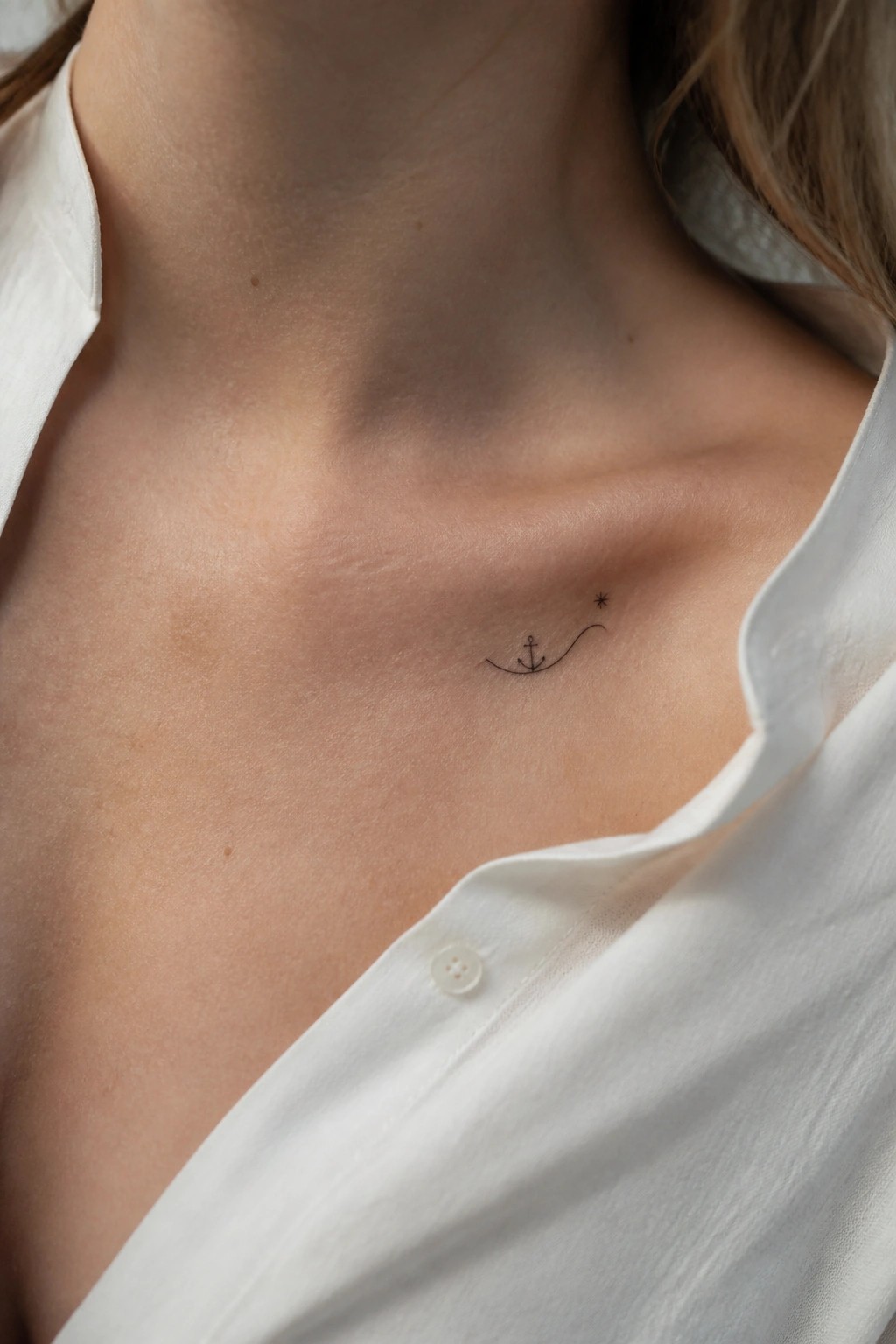 Small anchor tattoo with wave and stars on chest in white shirt