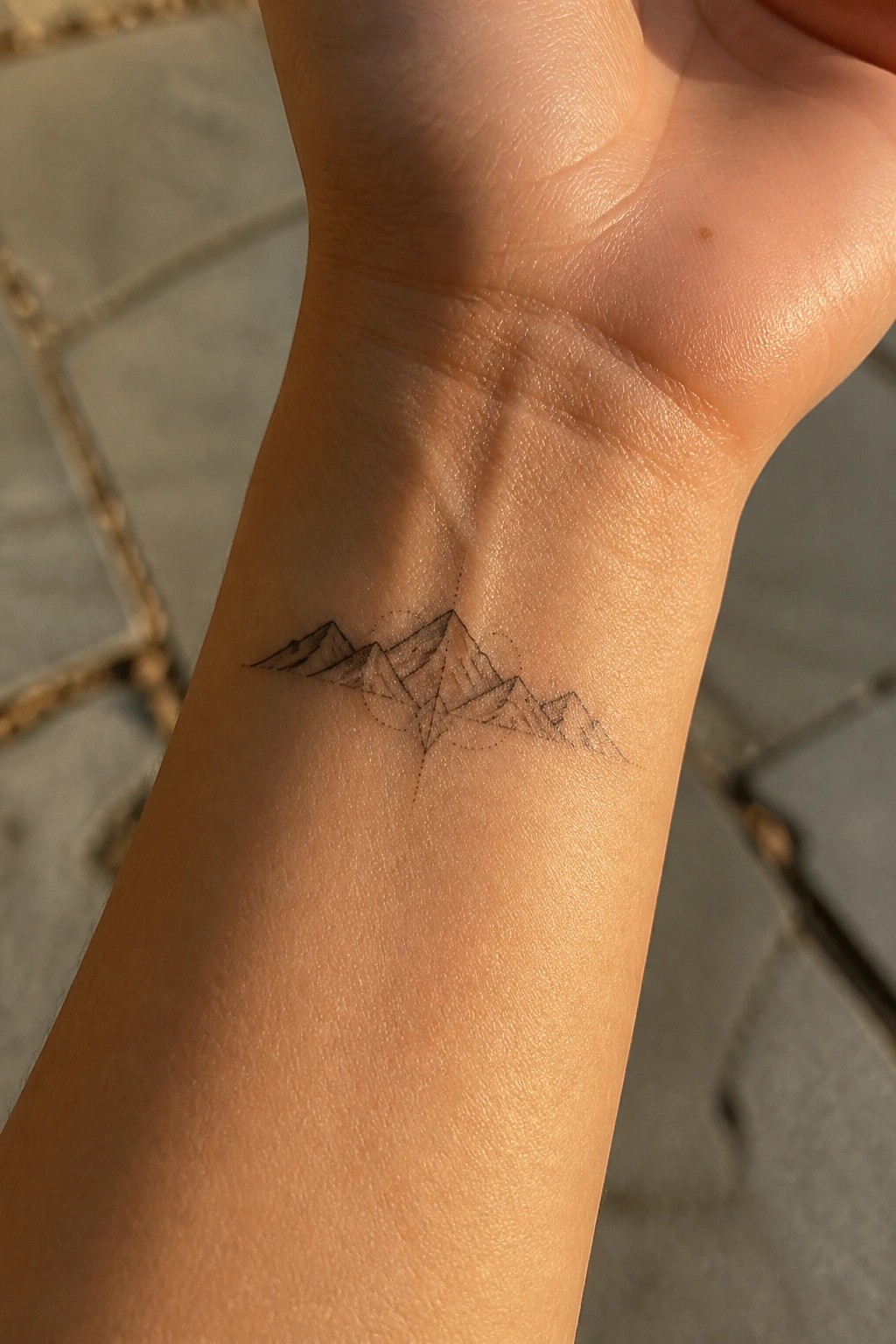 Geometric black mountain tattoo on inner wrist with dotted accents