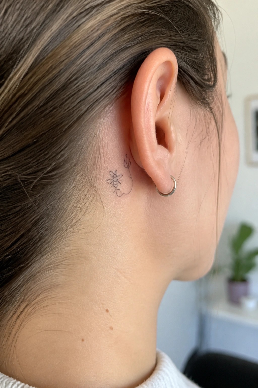 Close-up of ear with bee and flower line tattoo and silver hoop earring.