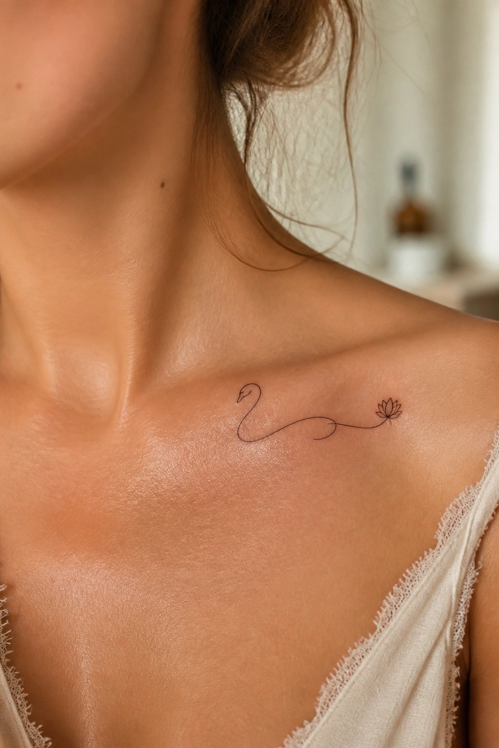 Swan and lotus tattoo on woman's collarbone above white lace top.