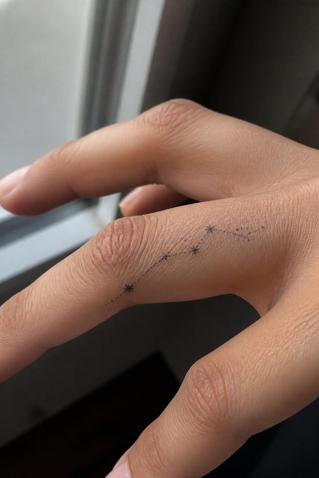 Hand with black constellation tattoo of stars connected by dotted lines on skin.