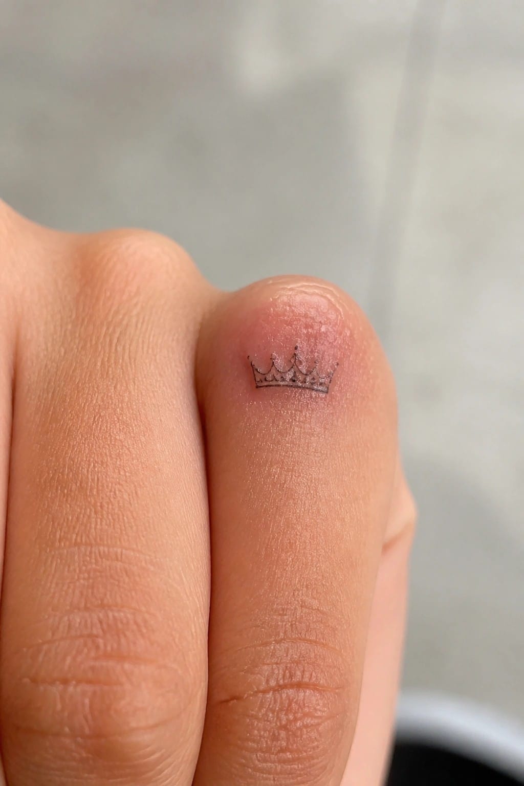 Small black crown tattoo on fingertip with visible skin texture and ridges.