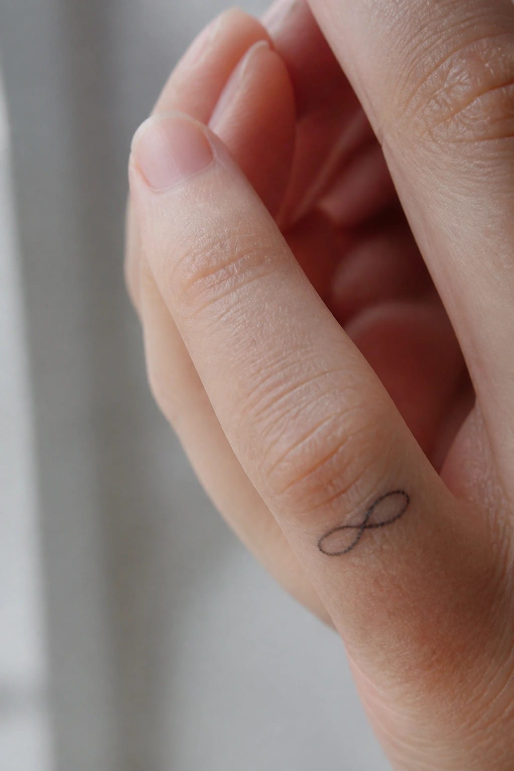 Small infinity symbol tattoo placed along the side of a finger