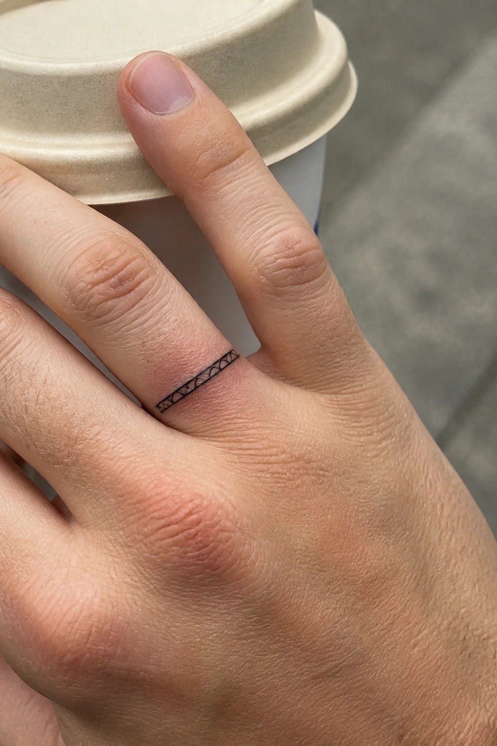 Close-up of a thin black geometric band tattoo wrapped around the base of a ring finger.