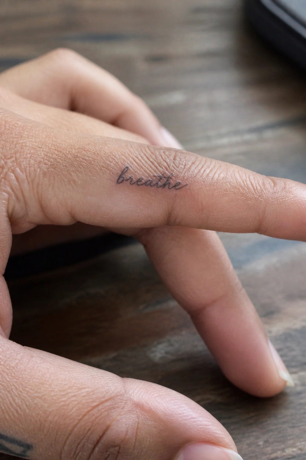 Small cursive tattoo of the word breathe on the side of a finger