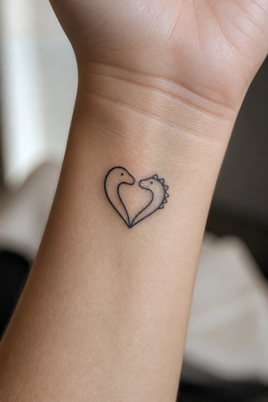 Black line tattoo of two dinosaurs forming a heart on a wrist