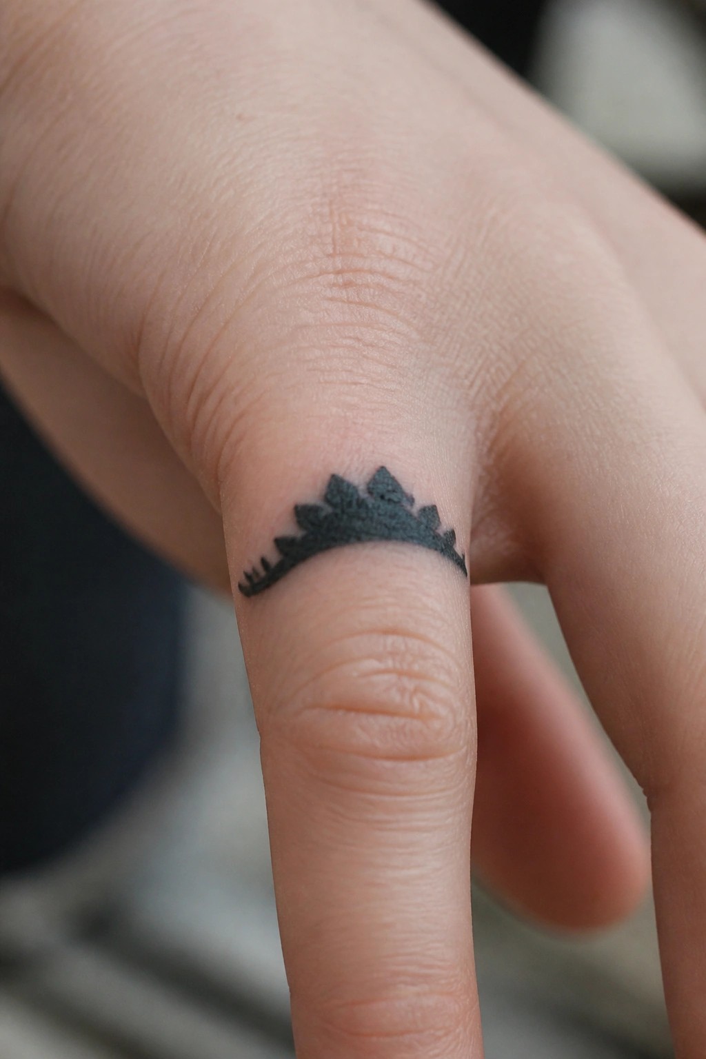 Close-up of a small black dinosaur-spine tattoo on a light-skinned finger.