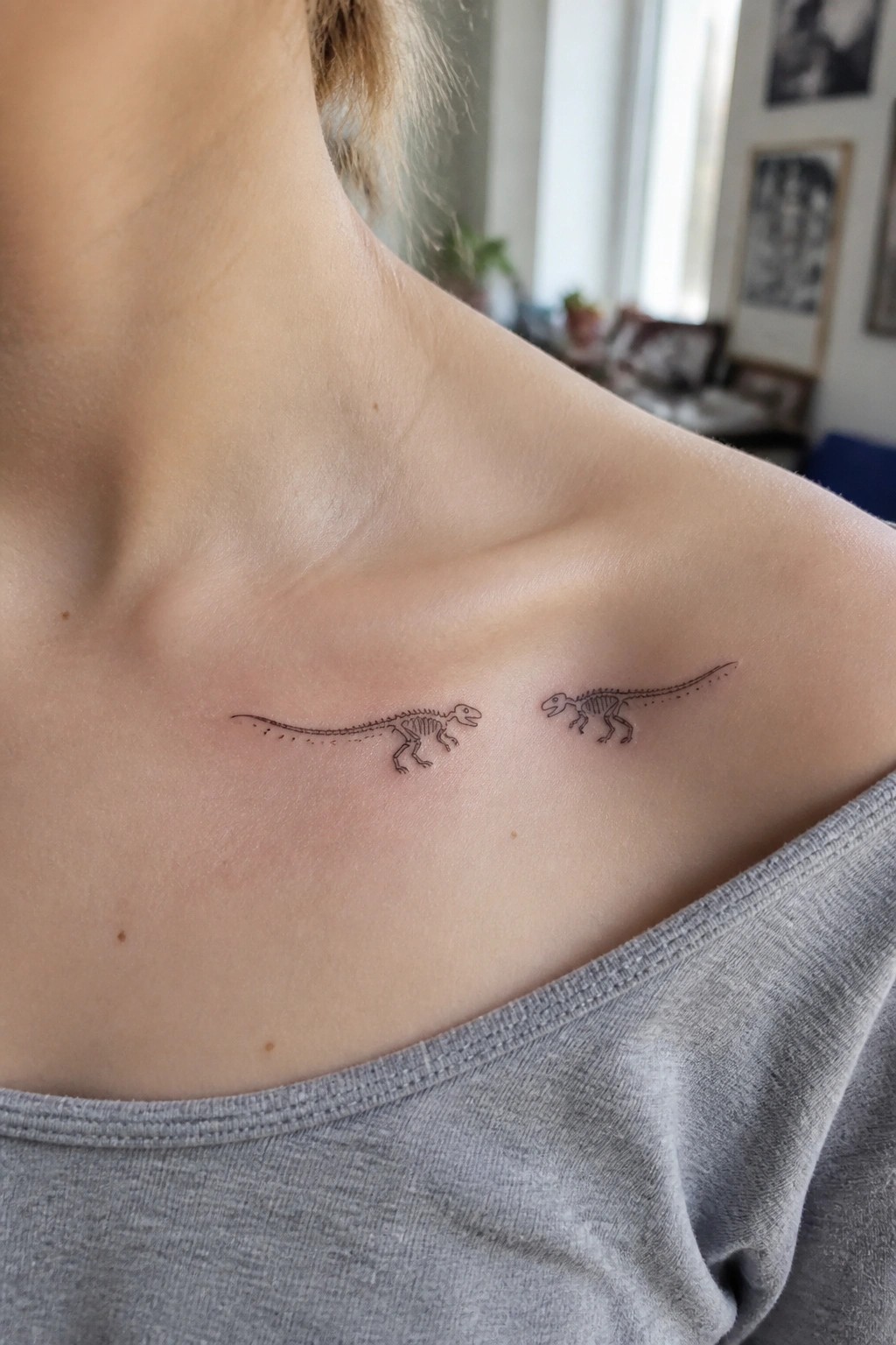 Two dinosaur skeleton tattoos on shoulder of person in gray off-shoulder top