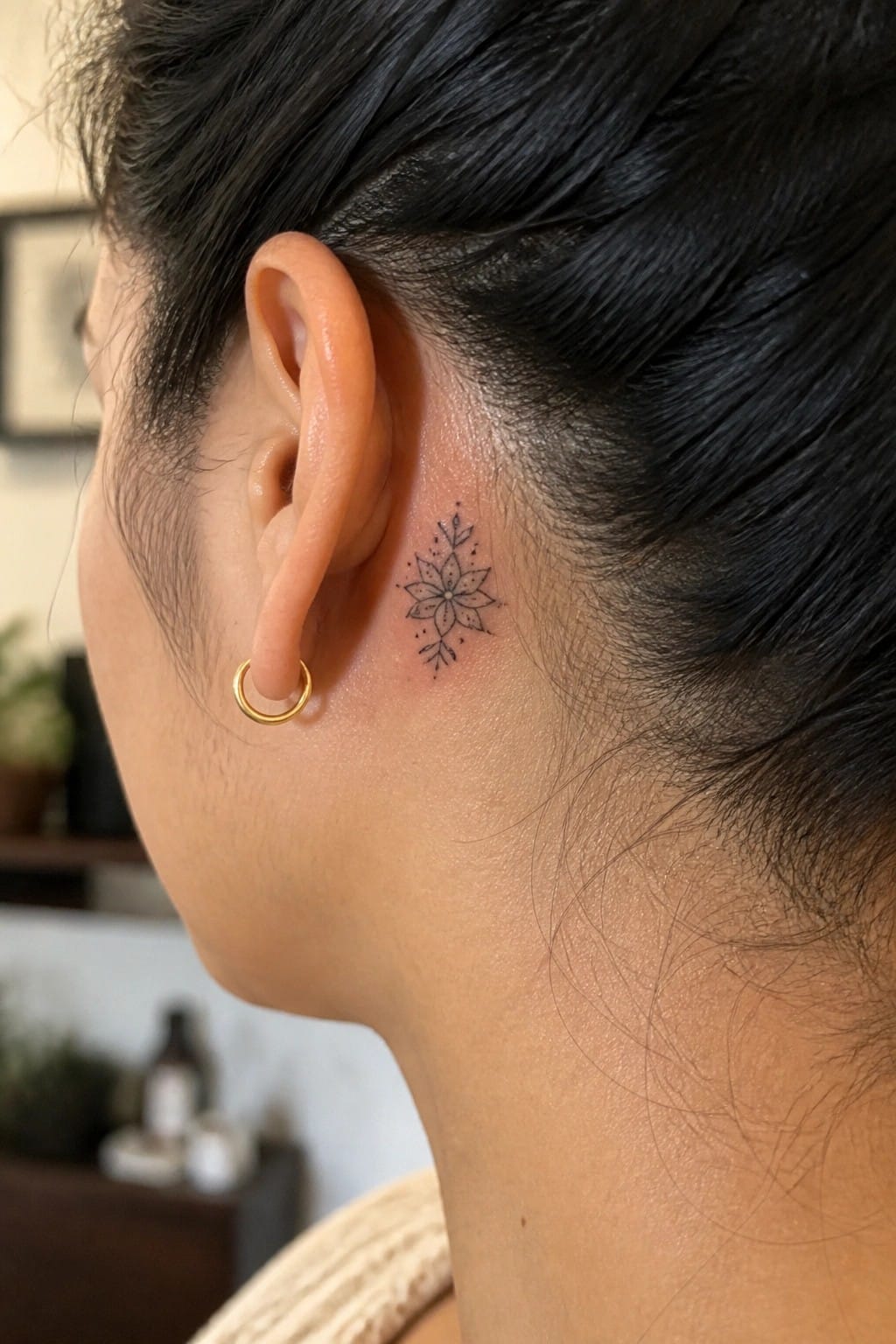 Close-up of small black mandala tattoo behind ear with gold hoop earring and dark hair.