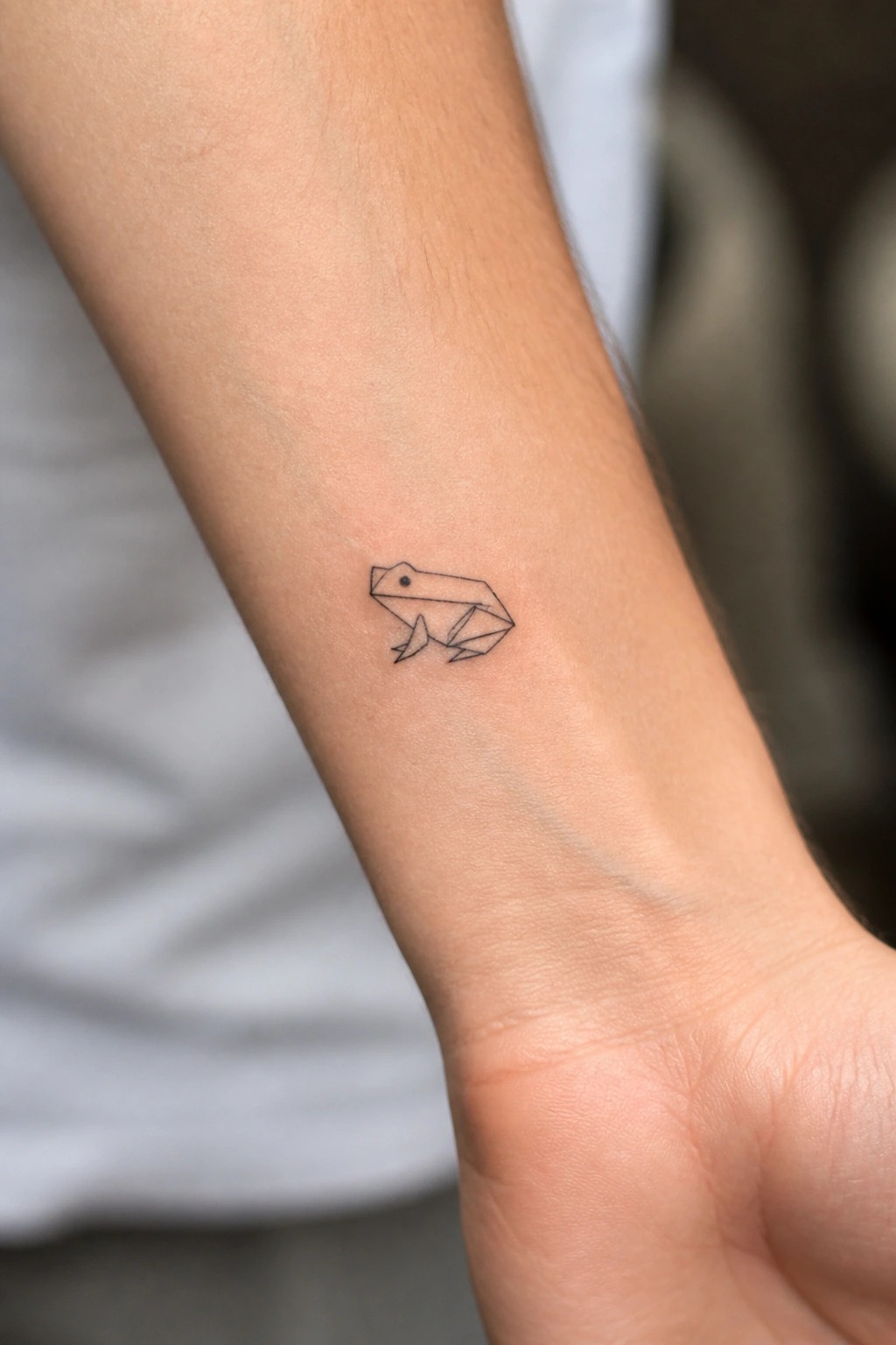 Minimalist line drawing of a frog tattoo on the inner forearm