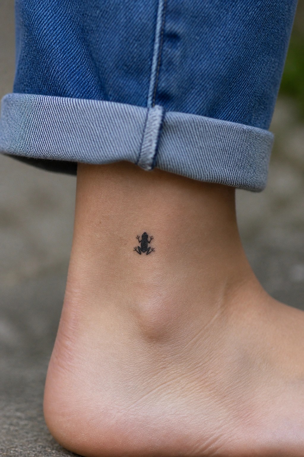Small black frog tattoo on ankle below rolled blue jean cuff