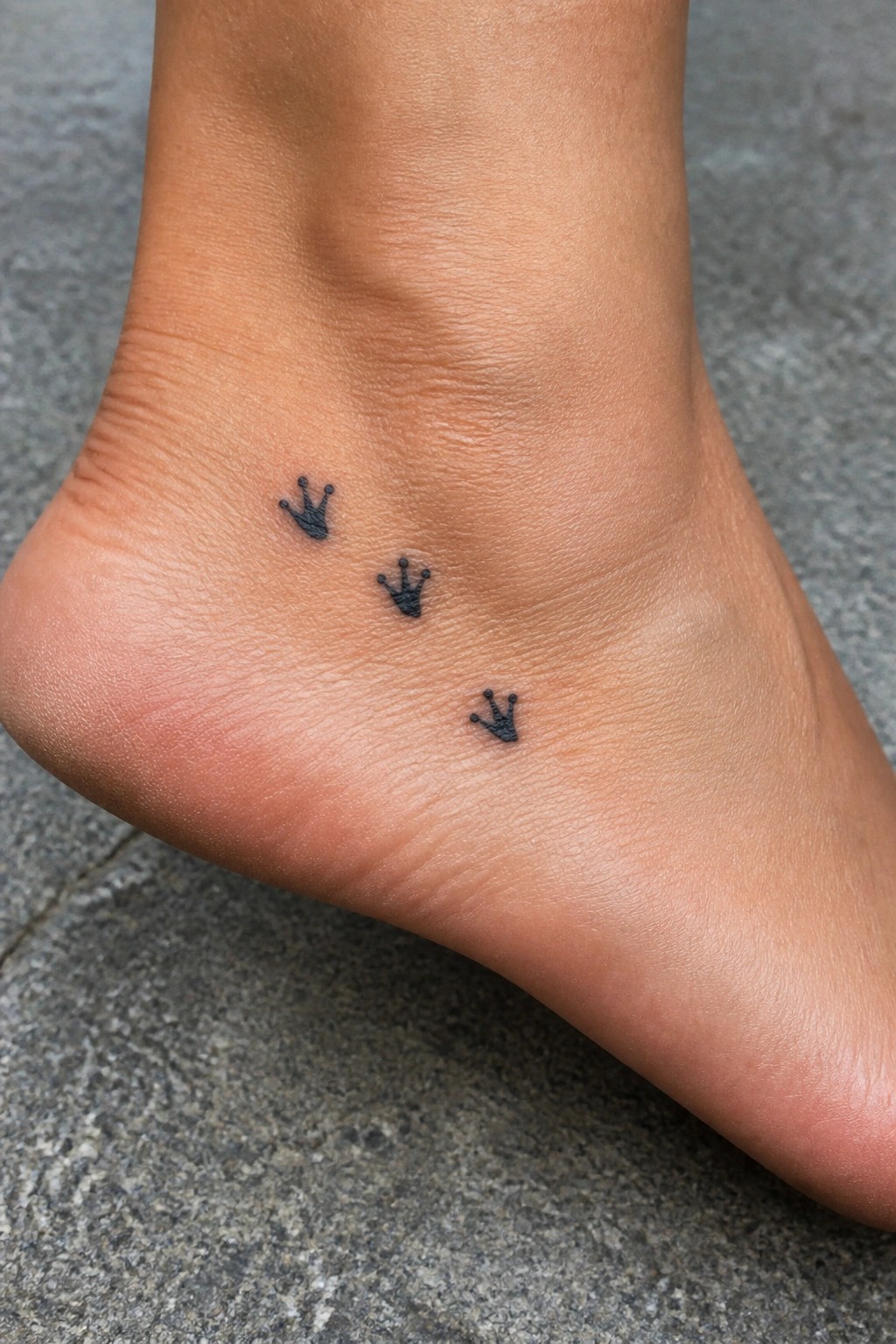 Three small black crown tattoos on light-skinned ankle and foot
