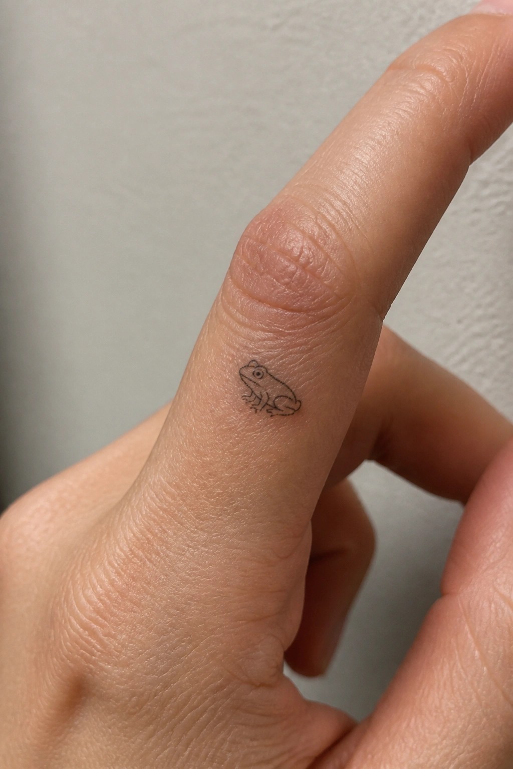 Small black frog tattoo on the side of a light-skinned finger
