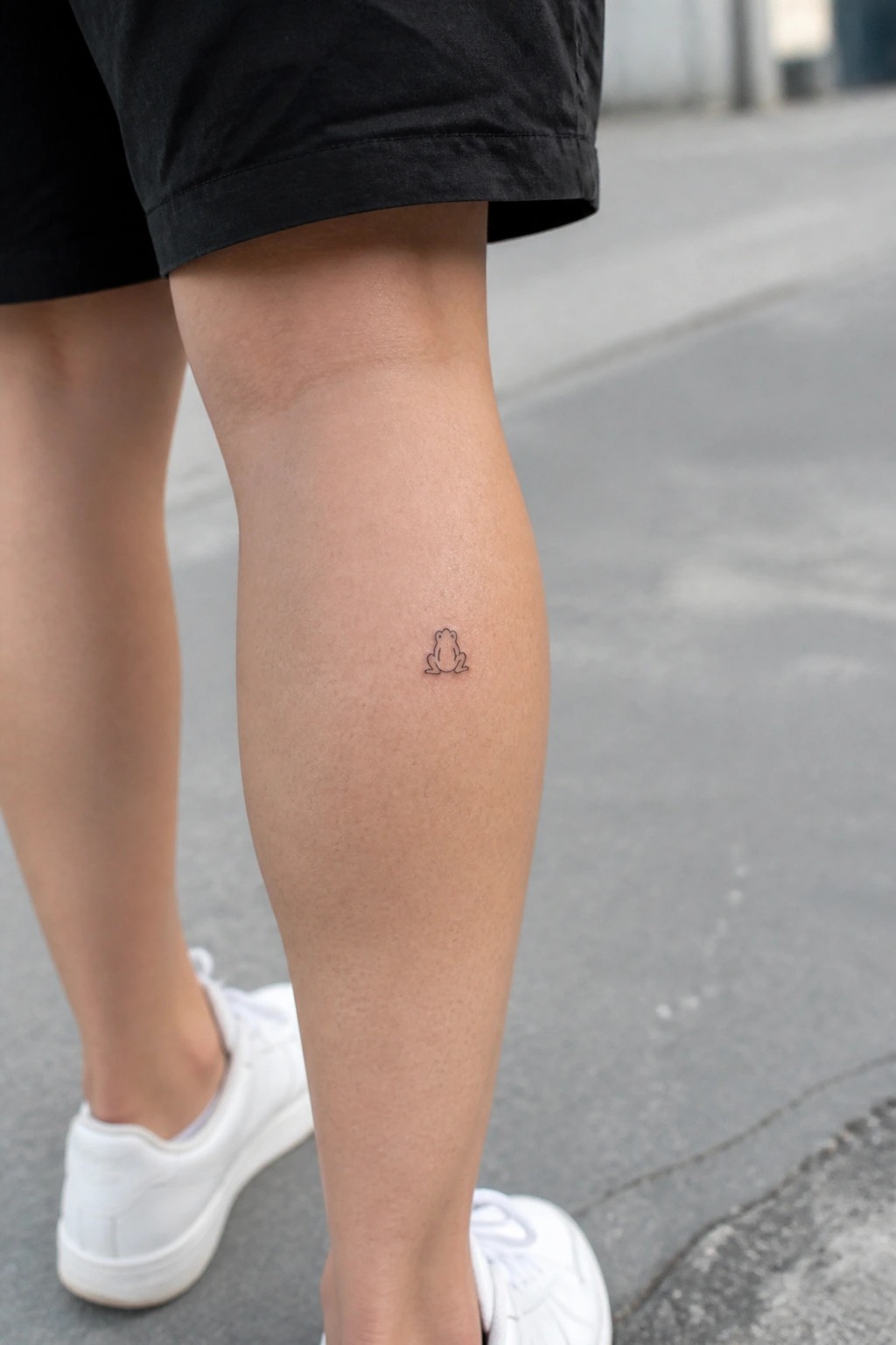 small minimalist frog tattoo on the shin in simple black outline style