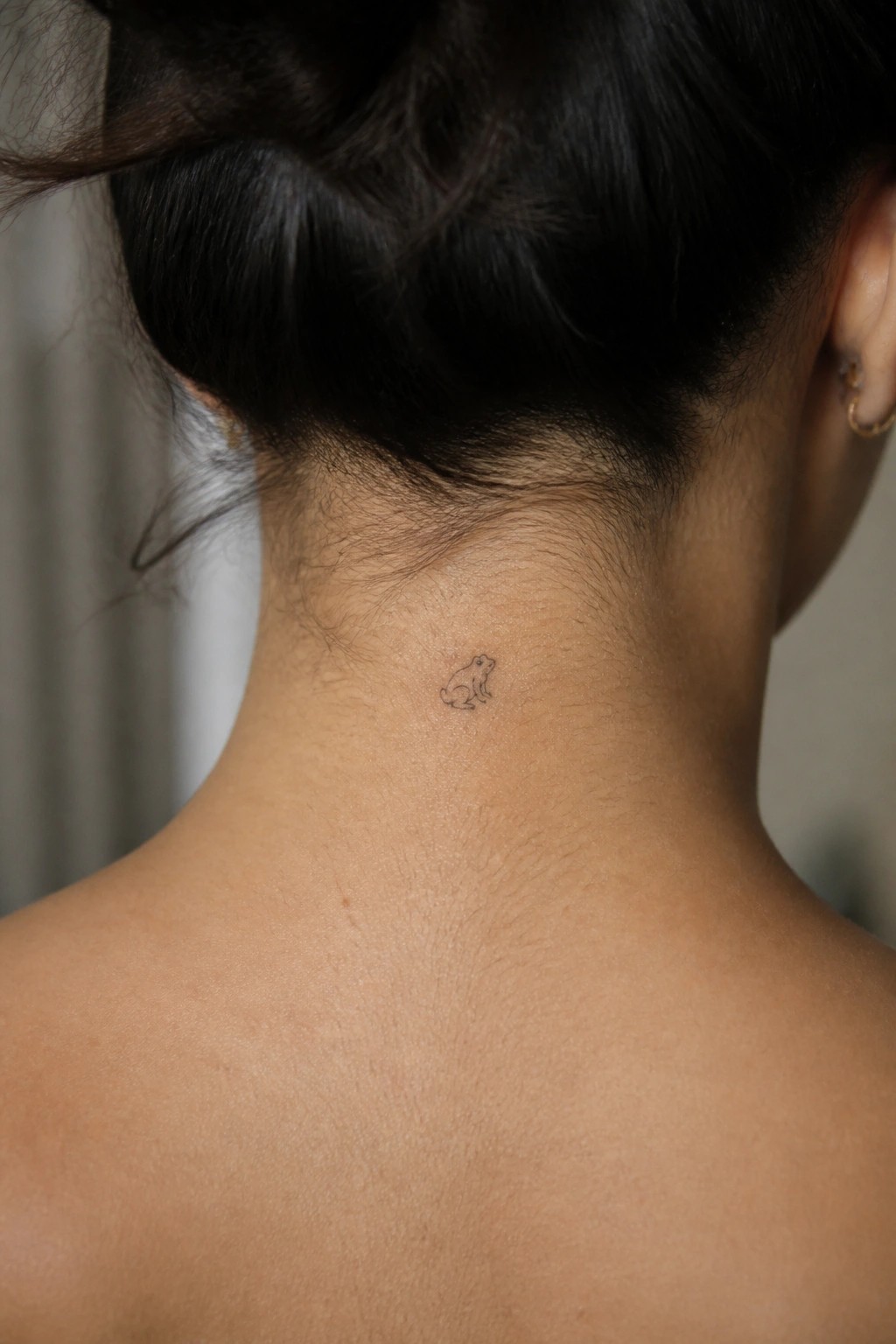 Small frog tattoo on nape of neck with dark hair in bun