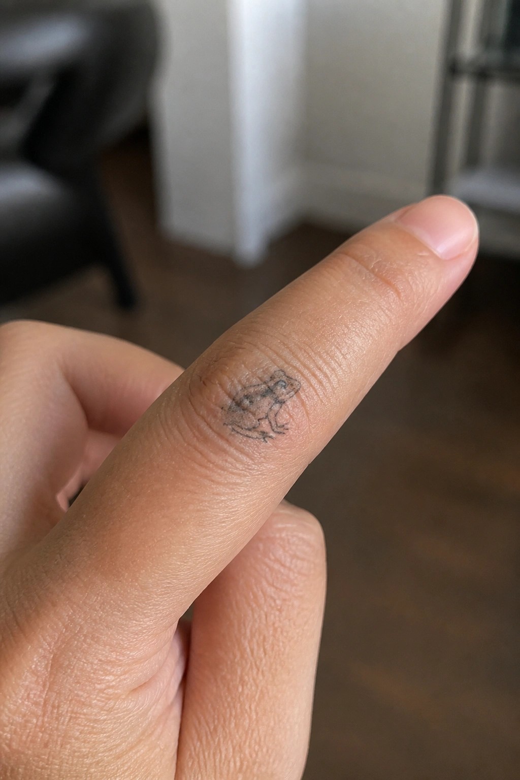 Small line drawing of a frog tattooed on the side of a finger near the knuckle