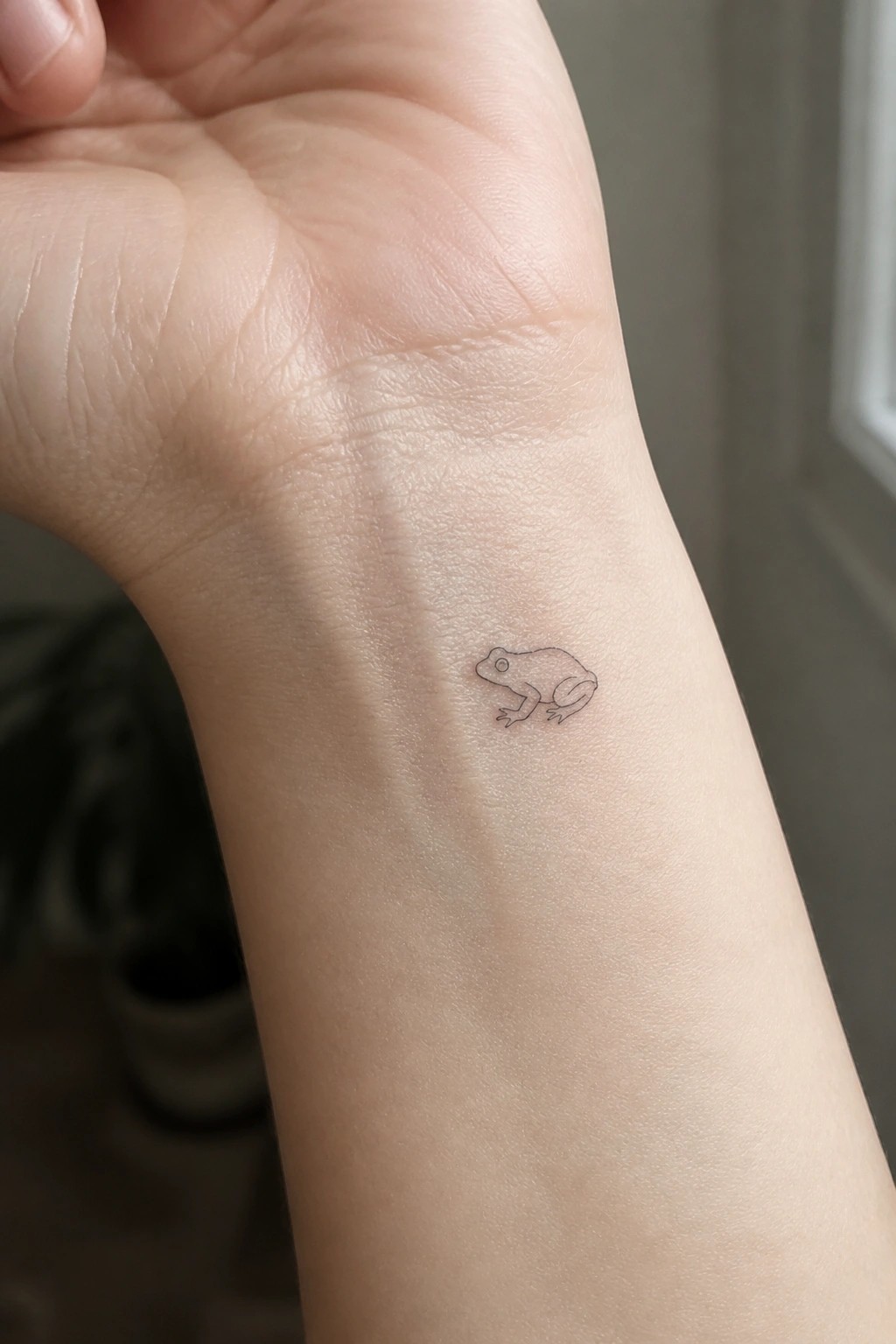Small minimalist frog tattoo on inner wrist of light-skinned hand
