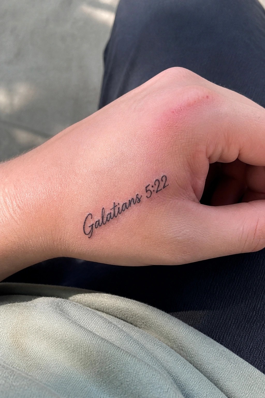 Hand with Galatians 5:22 tattoo and red mark on blue-green clothing
